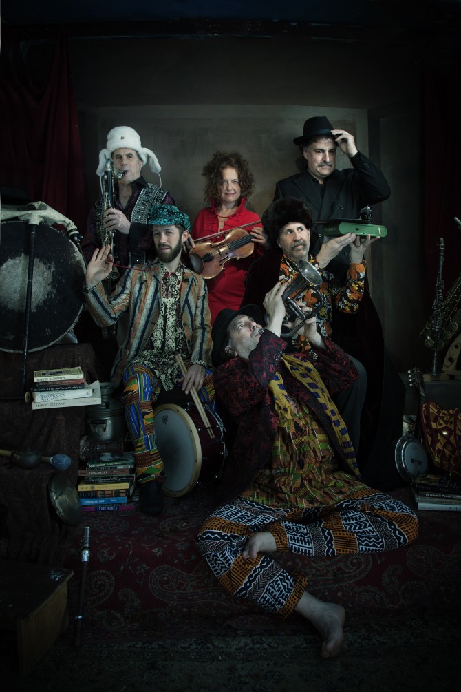 Six people, members of a musical group, pose in dark-colored costumes