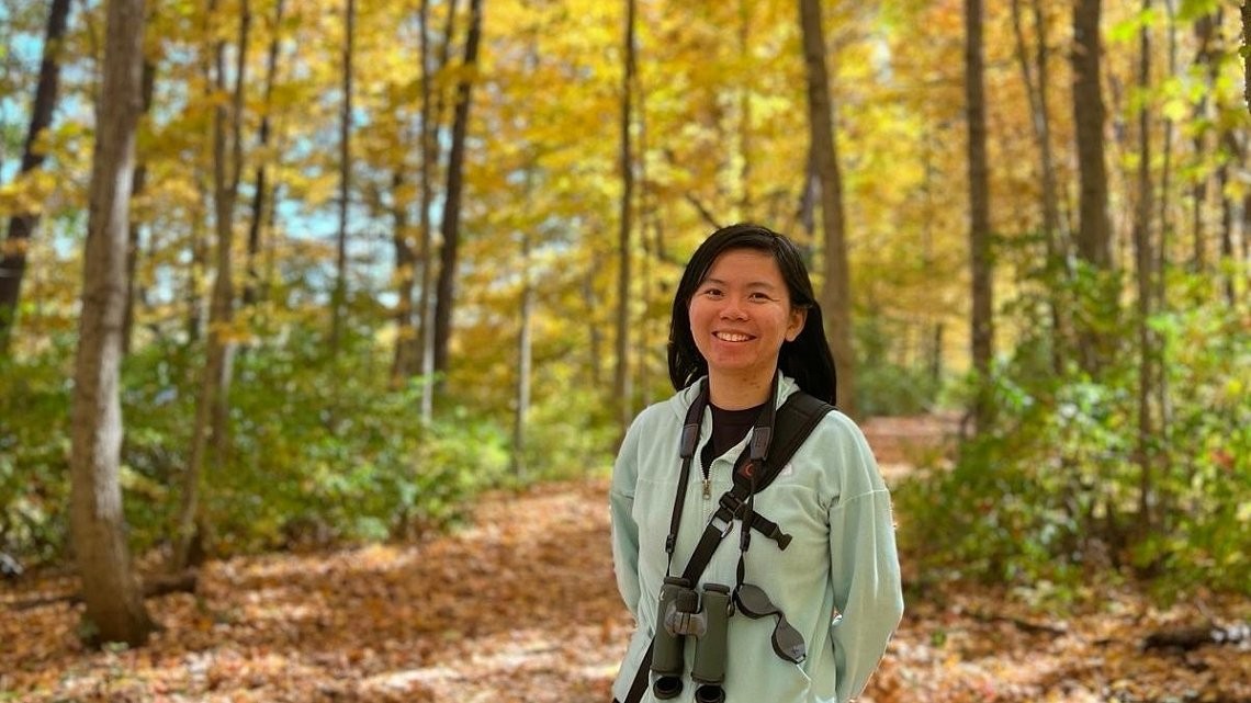 smiling female in wooded area with camera