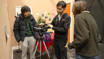 Three students look at video camera on tripod
